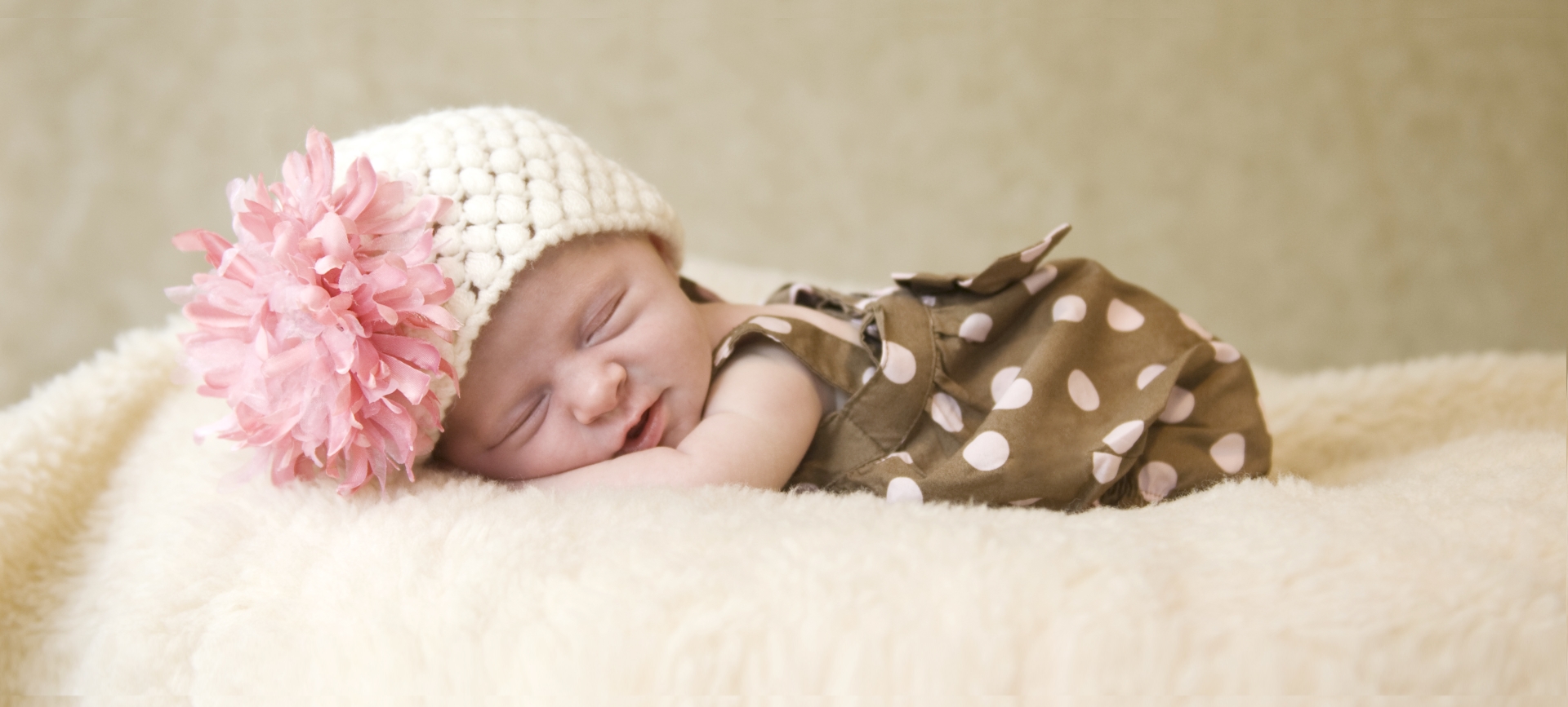 Newborn laying on fur blanket with flower hat.